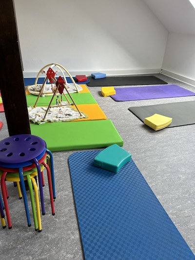 Raum mit Gymnastikmatten und Baby-Spielbogen.