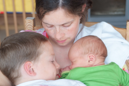 Ein großes Kind und ein Säugling kuscheln sich an ihre Mutter